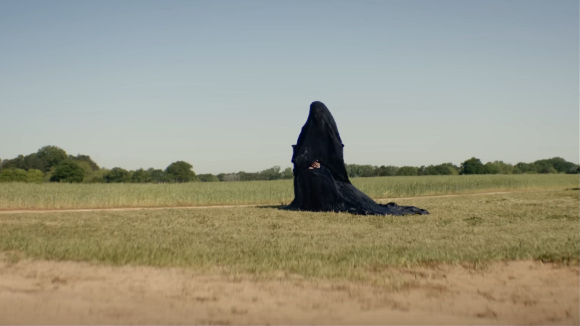 The Woman in the Yard appears motionless and spectral in a field, embodying the physical manifestation of Ramona’s darkest thoughts. (Image via Universal/Youtube)
